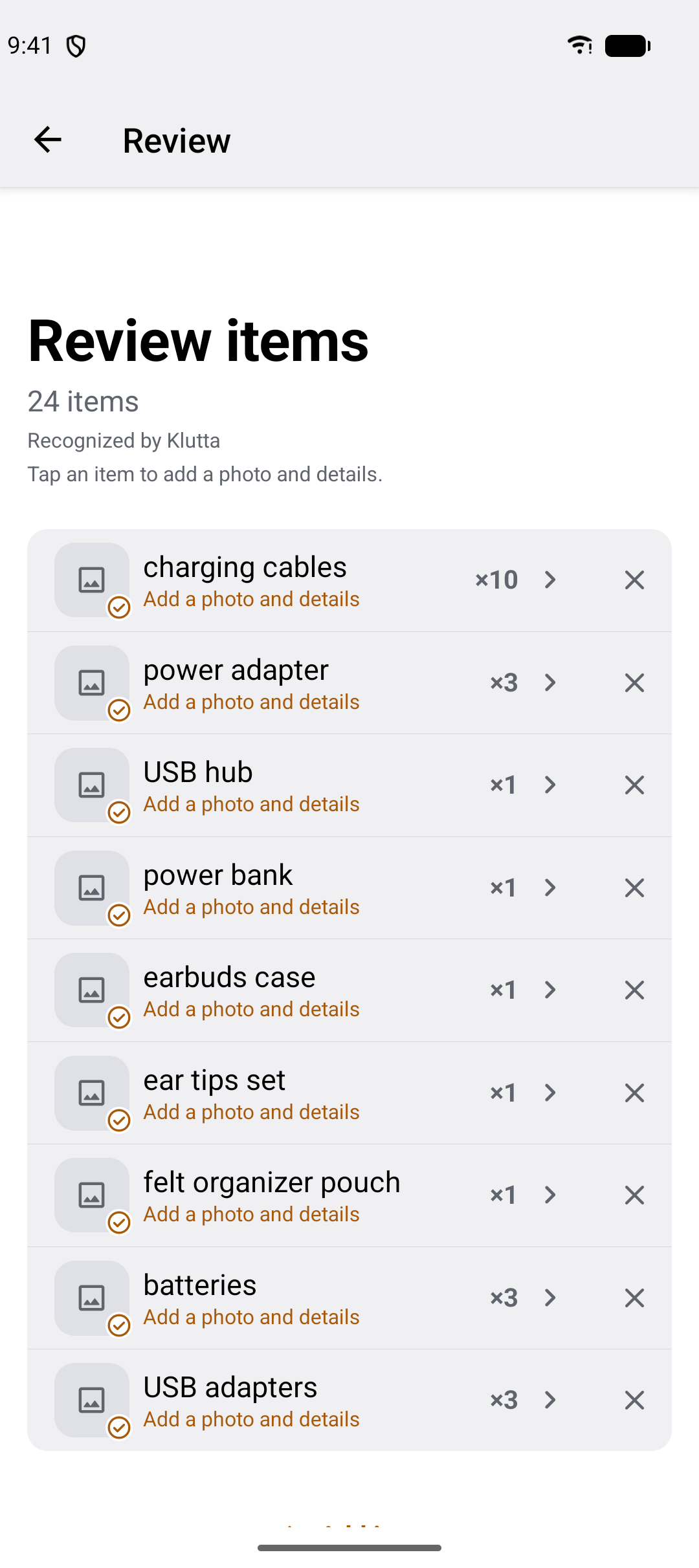 The review screen: Review items, 24 items, recognized by Klutta, and a list of rows — charging cables times 10, power adapter times 3, USB hub, power bank, earbuds case — each with a chevron to add a photo and details and a cross to remove it.
